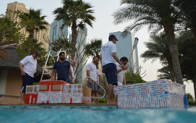 A team carrying the cardboard boats they built down to the water