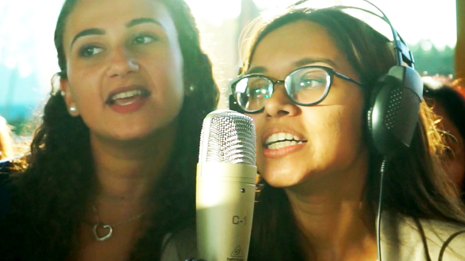 Two participants singing into the studio microphone while recording the company song