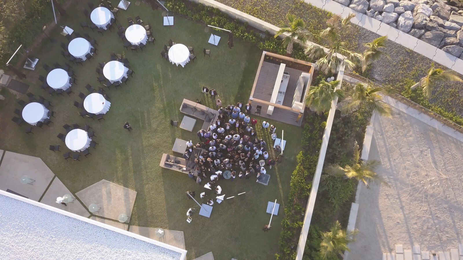 A company event seen from above, banquet tables on the lawn and the group gathered by the sea