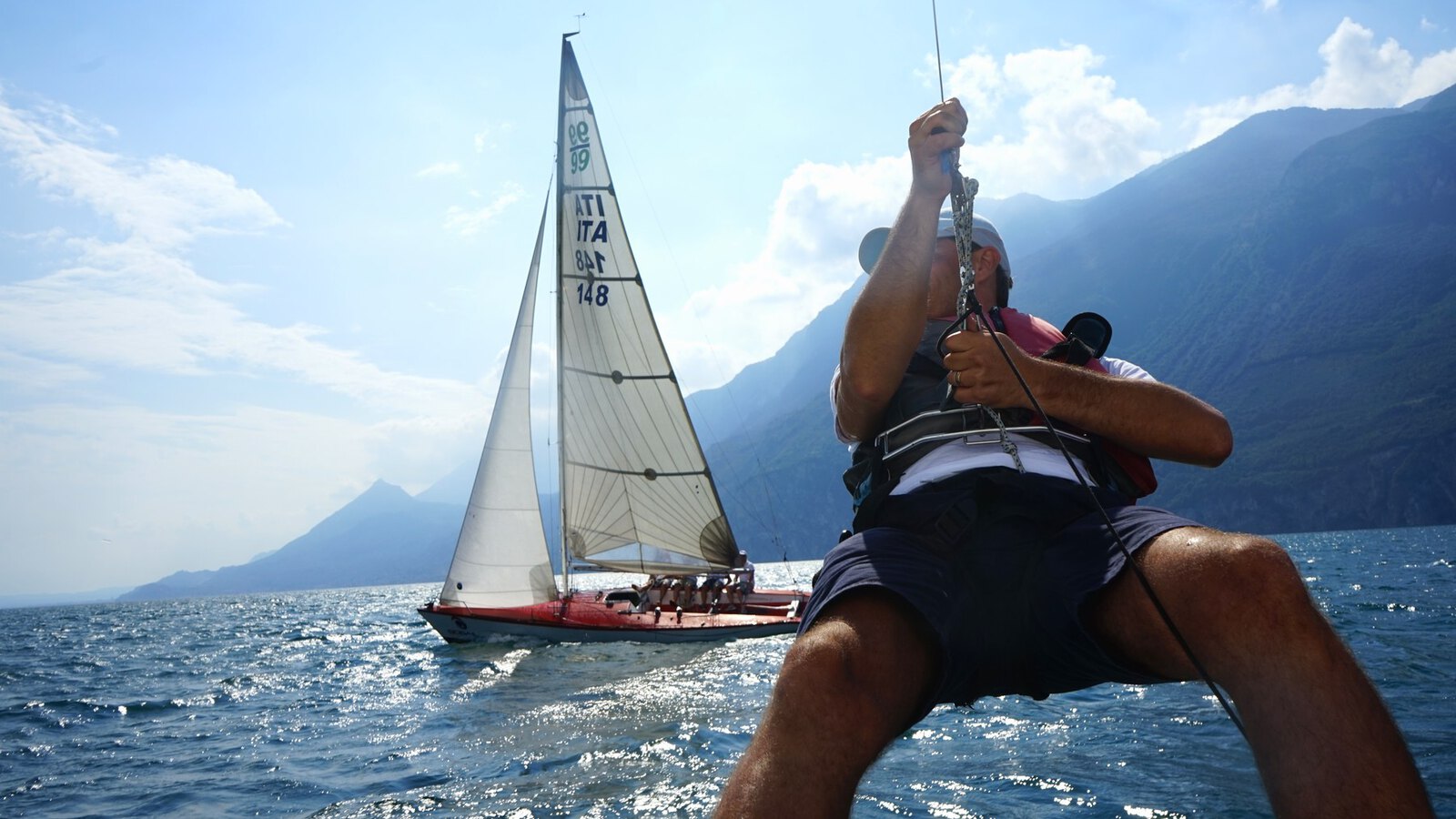 A sailing crew trimming the sail while the boat ahead holds its course
